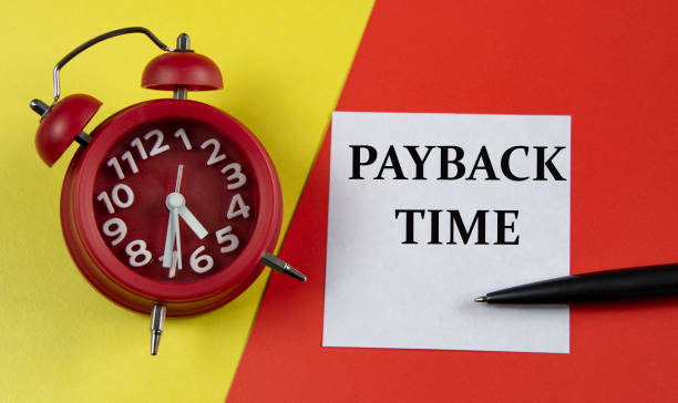 istock PAYBACK TIME - words on a white sheet on a multi-colored background with an alarm clock and a pen 1316401091