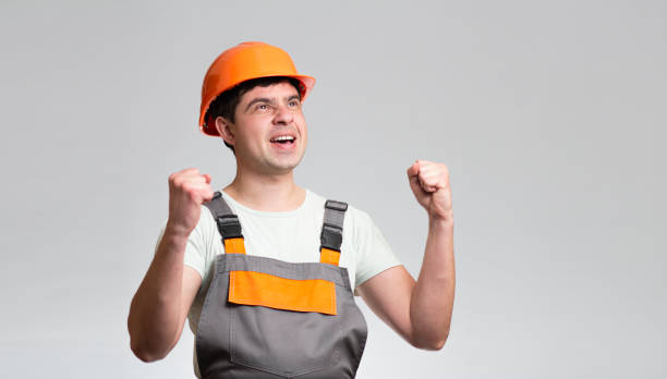 istock jubilant young foreman in hardhat and overalls, builder rejoices on grey studio background 1316403330