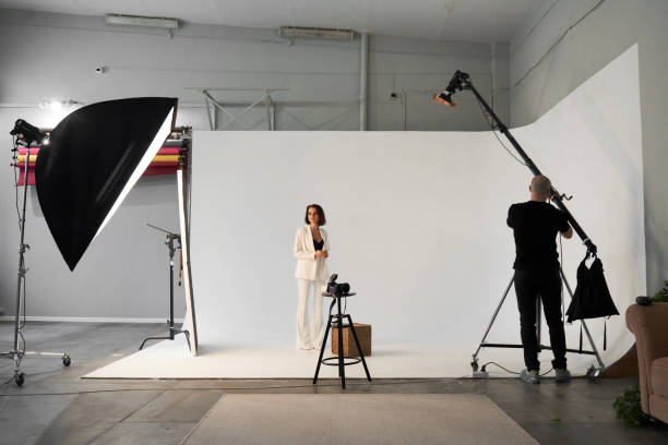 photographie de mode dans un studio photo. photographe masculin professionnel prenant des photos du beau modèle de femme sur l’appareil-photo, en coulisses - séance photo photos et images de collection