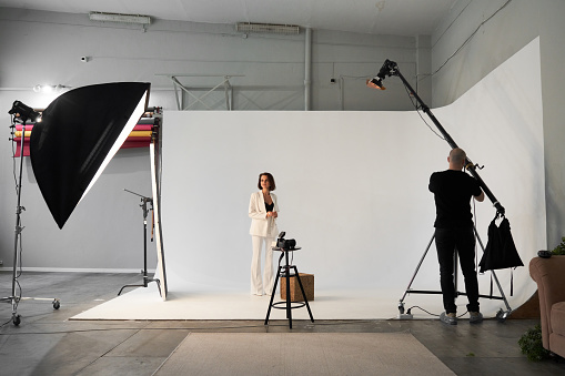 Fashion photography in a photo studio. Professional male photographer taking pictures of beautiful woman model on camera, backstage