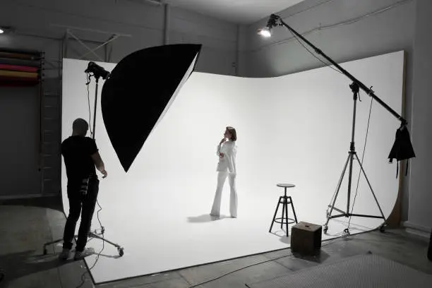 Photo of Fashion photography in a photo studio. Professional male photographer taking pictures of beautiful woman model on camera, backstage