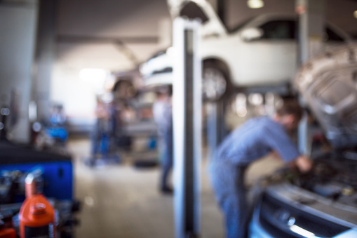 Car repair service in defocus, industrial background. Cars on lifts, transport service area, the mechanic repairs the car. Copy space