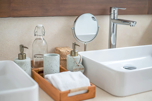 Close-up shot of various toilet amenities on the bathroom counter of a luxurious hotel. They provided the guests with drinking water, clean glasses and towels, and liquid soap and body cream in ceramic dispensers.