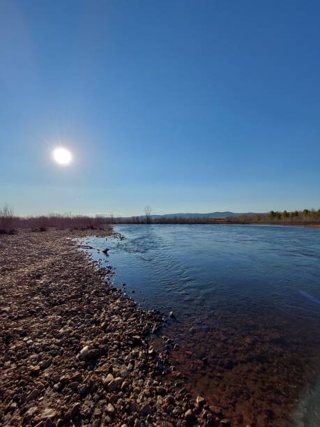 istock Spring River flowing River with pebble shore against blue sky and sun 1316411183