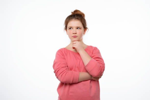 istock Young girl with thoughtful expression, keeps hand on chin, plans something or makes choice. Studio shot white background 1316412778
