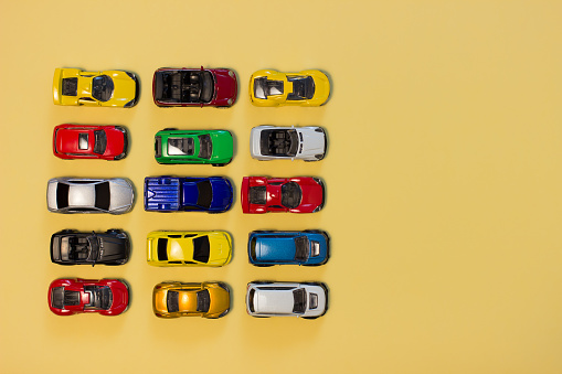 Colorful toy cars top view on a yellow background with copy space.