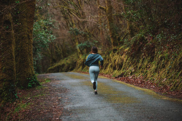 istock Woman running along road in forest 1316415422