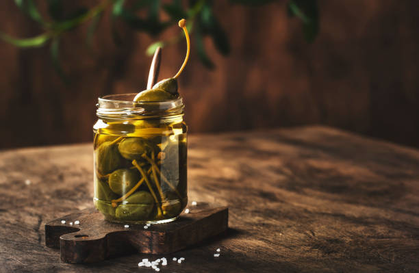 istock Capers. Marinated or pickled canned capers fruit in glass jar on wooden table, eco style still life 1316418082