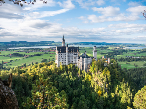 09/24/2020 Schwangau, Bavaria, Germany.\nSide angle view of Neuschwanstein castle in Autumn, forest surrounding it.\nSunny day