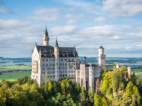 09/24/2020 Schwangau, Bavaria, Germany.\nSide angle view of Neuschwanstein castle in Autumn, forest surrounding it.\nSunny day