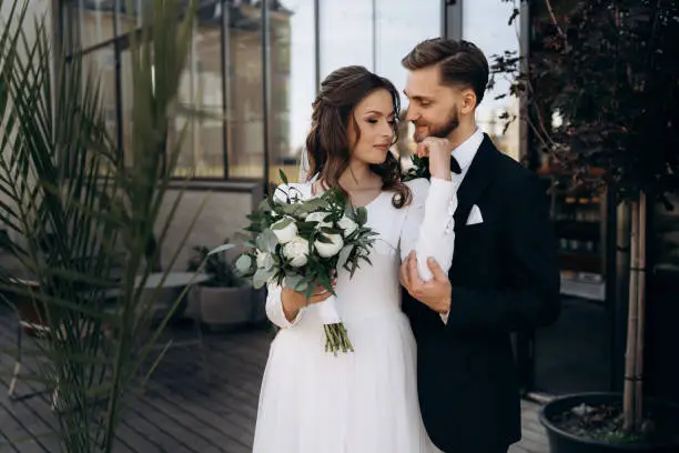 The groom hugs the bride. Portrait of a cute European newlyweds near palm leaves. Wedding outdoors