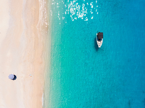 Aerial top down view to a secluded paradise beach on the island of Kefalonia with a moored boat over the clear, turquoise sea