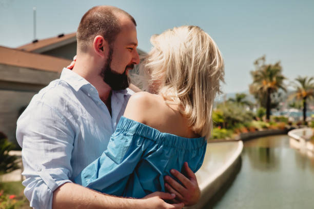 loving couple enjoying honeymoon in luxury hotel, walking through grounds with palm trees and swimming pool - honeymoon beach swimming pool couple imagens e fotografias de stock