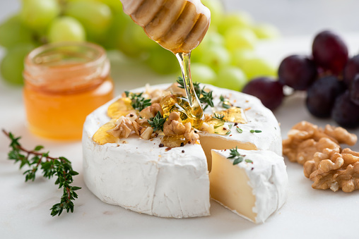 Honey pouring on camembert cheese with walnuts and grapes. Gourmet cheese appetizer brie or camembert with honey, nuts, fruits