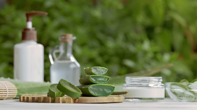 Panning shot of aloe vera slices and moisturizer on a wooden table. Beauty treatment concepts
