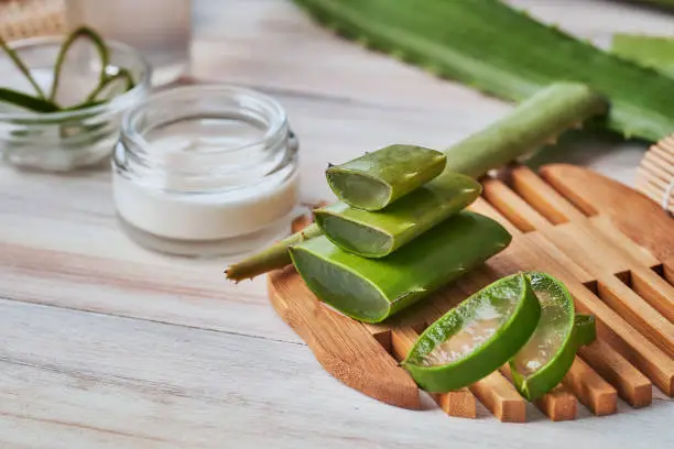 Photo of Aloe vera slices and moisturizer on a wooden table. Beauty treatment concepts