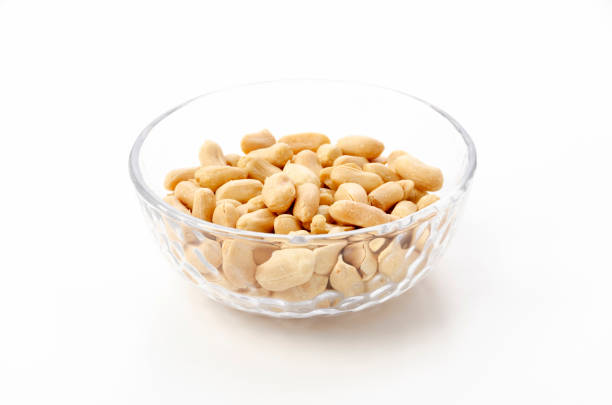 Roasted salted peanuts in a transparent glass bowl on a white background