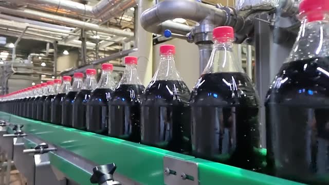 Dark liquid sweet soft drink moving at conveyor footage
