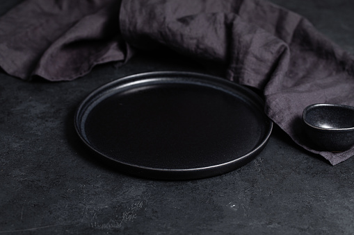 An empty stylish plate and gravy boat black on a black table background