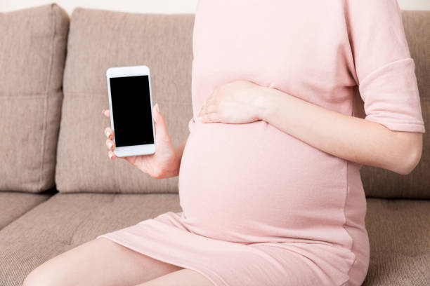 istock pregnancy with modern technologies.Pregnant woman showing cellphone with empty displayon sofa at home 1316432048