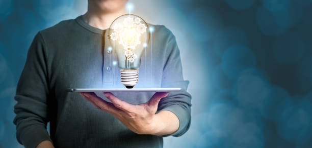 istock Man holding tablet computer with light bulb with cog wheel inside. Panoramic banner of creative idea with copy space 1316433369