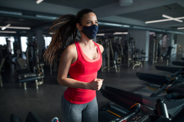 istock Woman with face mask doing exercise on treadmill in gym, coronavirus concept. 1316434585