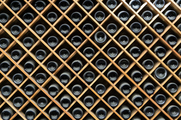 ワインボトルの背景。酒屋のワインキャビネットに入った赤と白のワインのボトル - ワイン貯蔵庫 写真 ストックフォトと画像
