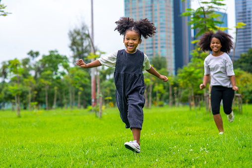 Happy mixed race family in park. Two Adorable little sibling sister running and playing together in public park. Adorable child girl kid enjoy and having fun outdoor lifestyle activity vacation.