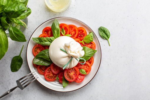 Burrata cheese with tomatoes and basil leaves. Caprese salad. Directly above, light table.