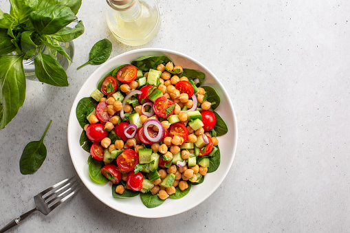 Fresh summer mediterranean salad with chickpea, tomatoes, cucumbers, spinach, red onion, parsley. Light background, copy space.