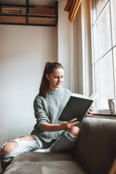 istock Modern Female Sitting On Living Room Sofa And Reading A Book 1316442043