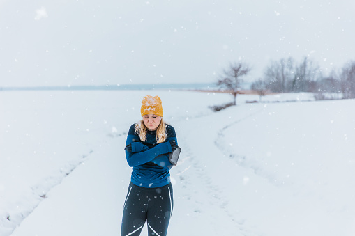 Woman in warm sportswear shivering and feeling cold in snow