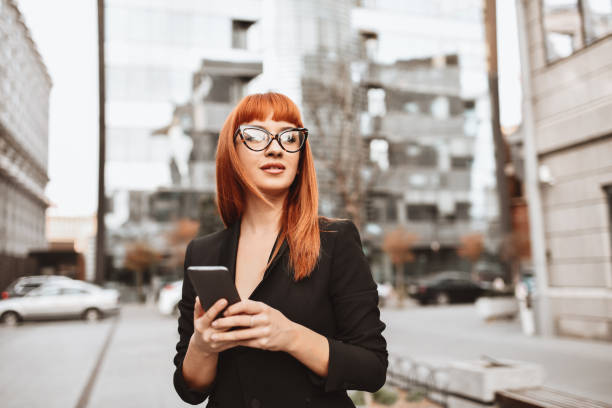 réunion élégante d’arrangement de femme d’affaires sur le smartphone tout en marchant dans la ville - mode bcbg photos et images de collection