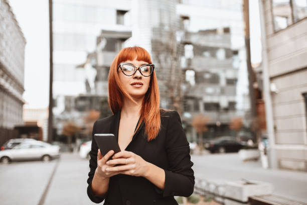 Elegant Businesswoman Arranging Meeting On Smartphone While Walking In City Elegant Businesswoman Arranging Meeting On Smartphone While Walking In City bangs hair stock pictures, royalty-free photos & images