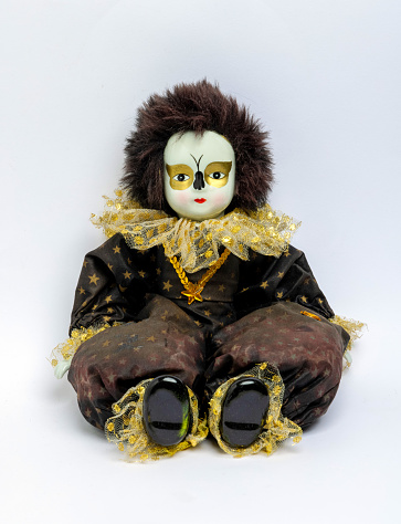 Old harlequin doll sitting against a white background