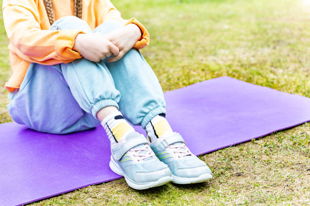 child sitting on a sports mat outdoors, hugging her knees with her arms. - healthy lifestyle nature sports shoe childhood imagens e fotografias de stock