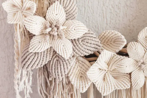 Photo of Macrame wreath with big cotton flower on a white decorative plaster wall. Natural cotton thread and rope. Eco decor for home. Creative greeting card for a creative person. Close up