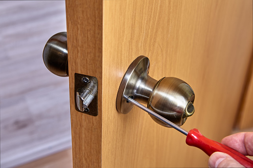Door handles with latch and lock are installed in new interior door, ball-shaped doorknob in bronze are repaired by locksmith.