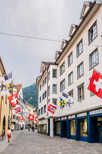 Flags of Switzerland and Grisons waving in Poststrasse in the historic district of Chur, the capital town of the Swiss canton of Graubunden. People strolling.
