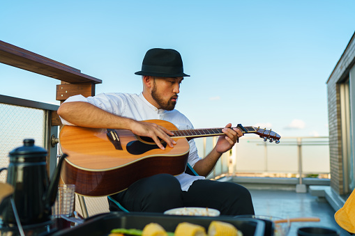 A young man is enjoying playing the guitar at the balcony at home.