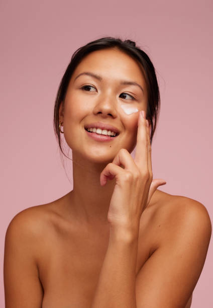 Beautiful woman applying moisturizer cream on her face Portrait of a beautiful woman applying moisturizer cream on her face. Woman using beauty product on her facial skin and looking away. face cream stock pictures, royalty-free photos & images
