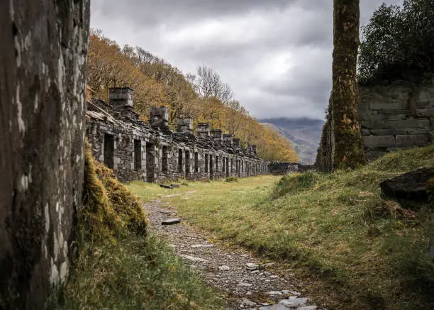 Photo of Row of abandoned old miners cottages in slate mine quarry Dinorwic North Wales. Eerie derelict barracks left behind on mountain top from old mining industry with overcast dramatic moody sky