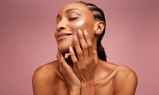 Close up of a female model applying moisturizer to her face. African american woman applying moisturizer cream on her face.