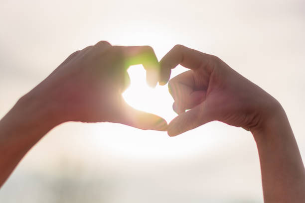 istock Woman making heart shape with hands against sky in sunlight 1316468785