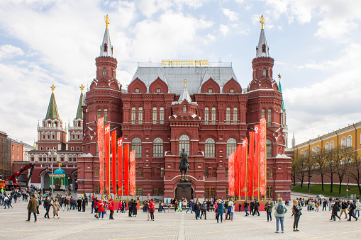 the brick building of the historical museum on Red Square, the monument to Marshal Zhukov and waving red flags on a cloudy day and walking tourists in Moscow Russia. May 9 Victory Day