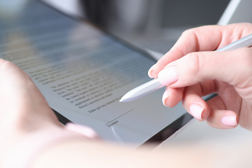 Woman hand holds stylus and puts an electronic signature in contract on tablet. Modern digital technology concept