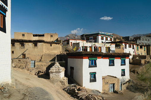 Kibber, India - September 16, 2019: Traditional village houses with flat roofs and Buddhist prayer flags flanked by Himalayas under blue sky on September 16, 2019 in Kibber, Himachal Pradesh, India.