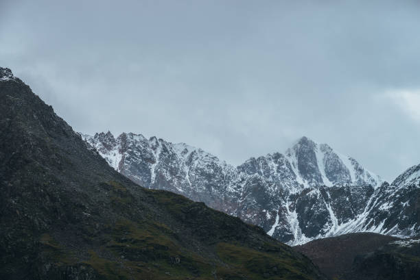 istock Atmospheric alpine landscape with great mountain peaked top with snow in low clouds. Dramatic mountain scenery with sharp pinnacle in overcast weather. Awesome view to snowy pointy peak in cloudy sky. 1316470451