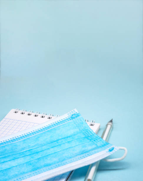 Medical mask and notepad on blue background. Stationery items and sanitary mask. stock photo