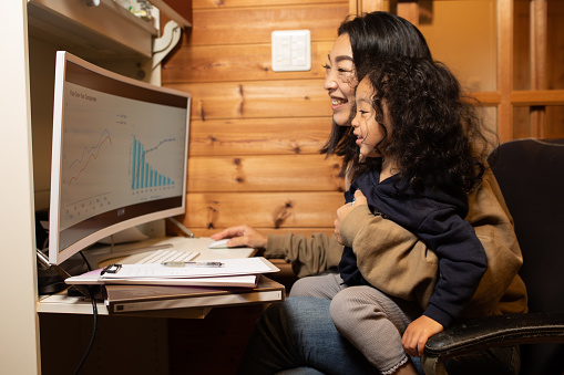 A Japanese single Mother is trying to get her work done from home on the computer while also looking after her young child.